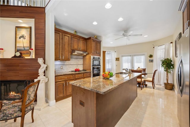 kitchen featuring ceiling fan, sink, backsplash, stainless steel appliances, and light stone countertops