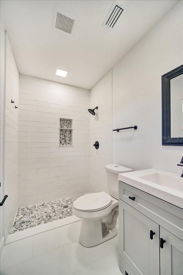 bathroom featuring vanity, tile flooring, a tile shower, and toilet