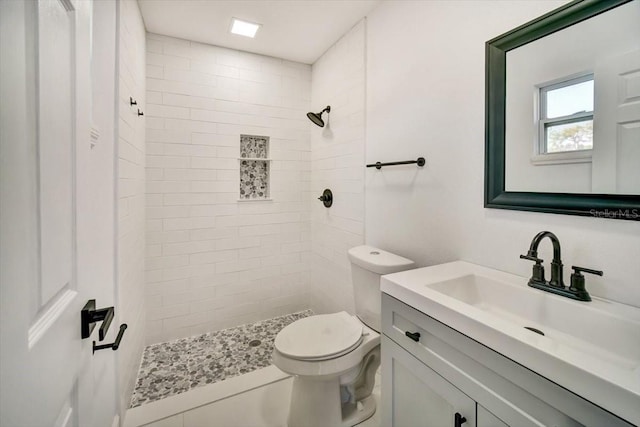 bathroom with toilet, a tile shower, and vanity