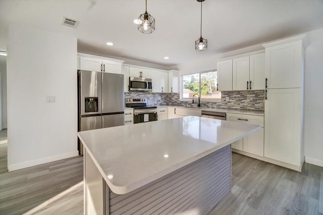 kitchen with light hardwood / wood-style flooring, backsplash, stainless steel appliances, white cabinetry, and a center island