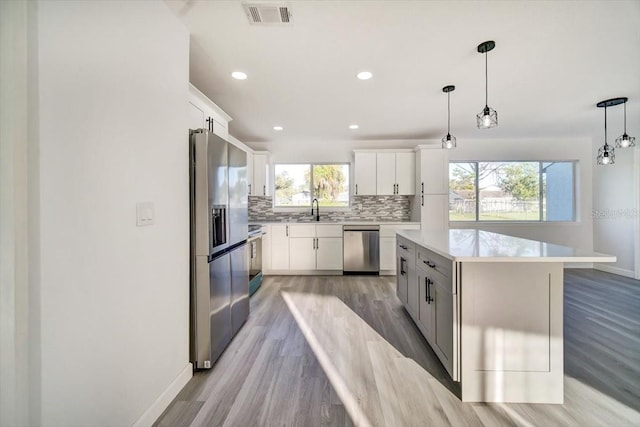 kitchen with light hardwood / wood-style floors, hanging light fixtures, stainless steel appliances, and a wealth of natural light