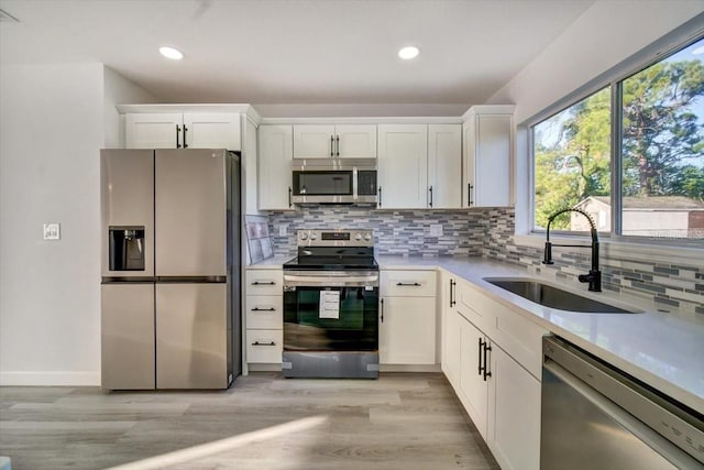 kitchen with appliances with stainless steel finishes, white cabinets, backsplash, light wood-type flooring, and sink