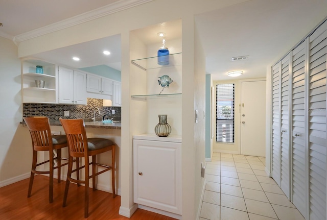 kitchen featuring a kitchen breakfast bar, light tile flooring, crown molding, white cabinets, and backsplash