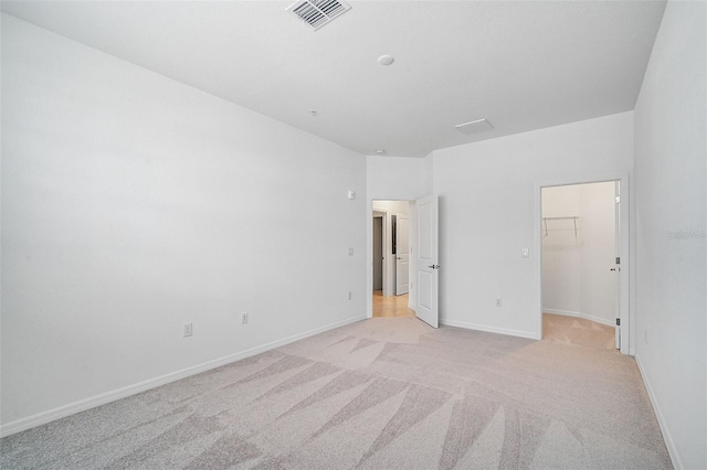 unfurnished bedroom featuring a spacious closet, light carpet, and a closet