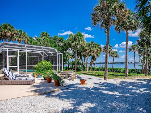 view of swimming pool featuring a patio, a water view, and glass enclosure