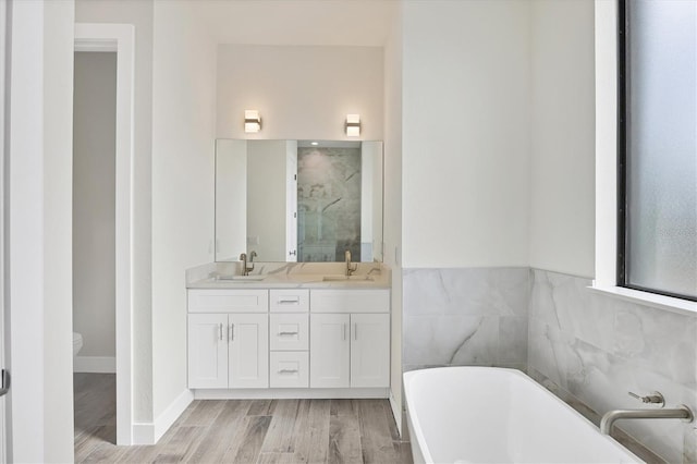 bathroom with a freestanding bath, double vanity, a sink, and wood finished floors