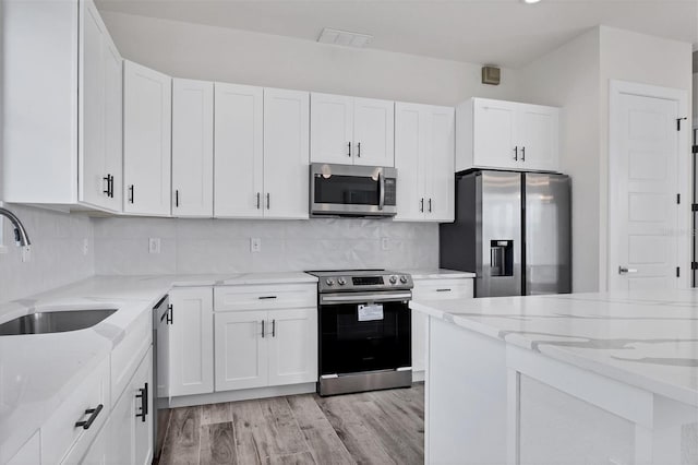 kitchen with light stone countertops, white cabinetry, stainless steel appliances, and a sink