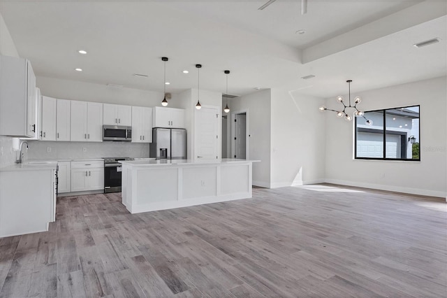 kitchen with white cabinetry, appliances with stainless steel finishes, decorative light fixtures, a kitchen island, and light wood-type flooring