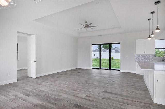 unfurnished living room featuring light wood-style floors, a tray ceiling, and baseboards