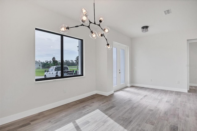 unfurnished dining area with a chandelier, french doors, light wood-type flooring, and plenty of natural light