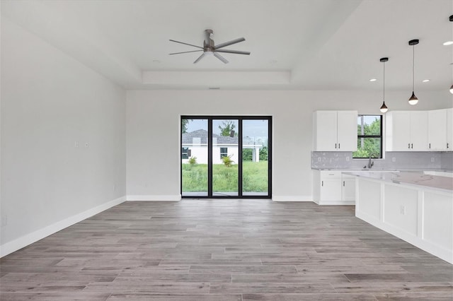 kitchen featuring white cabinets, decorative light fixtures, light hardwood / wood-style floors, and light stone counters