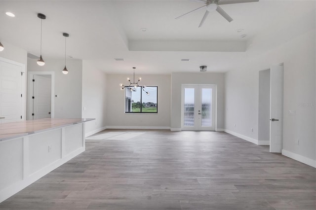 unfurnished living room featuring a tray ceiling, french doors, light hardwood / wood-style floors, and ceiling fan with notable chandelier