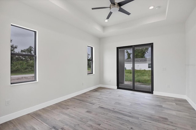 spare room with light wood-type flooring, baseboards, a tray ceiling, and recessed lighting