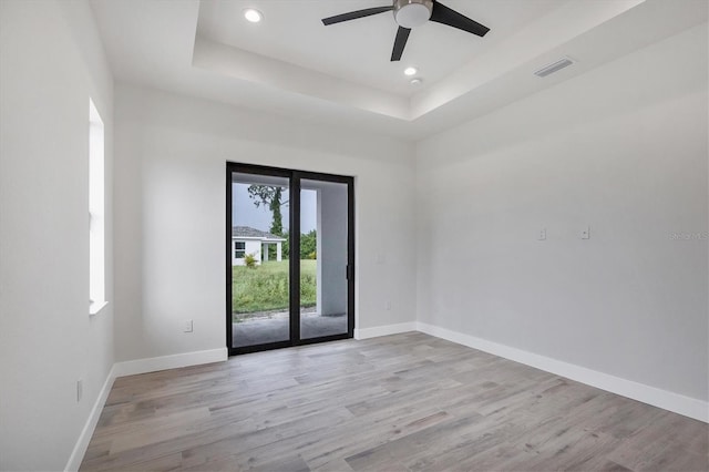 empty room featuring light wood-type flooring, a raised ceiling, visible vents, and baseboards