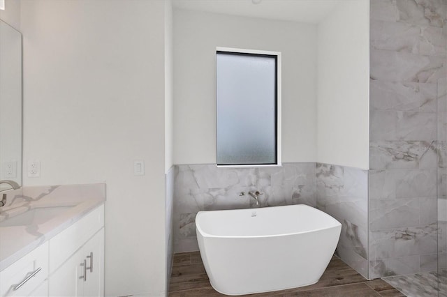 bathroom with wood finished floors, a freestanding tub, vanity, and tile walls