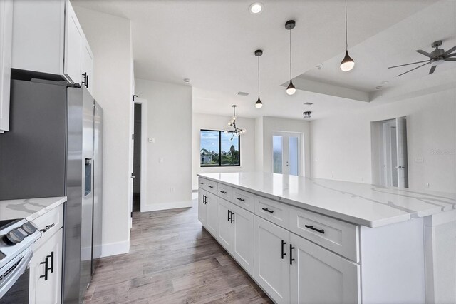 kitchen featuring appliances with stainless steel finishes, light wood-type flooring, light stone counters, decorative light fixtures, and white cabinets