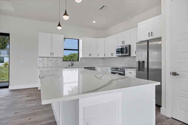 kitchen with white cabinets, a center island, stainless steel appliances, and hanging light fixtures