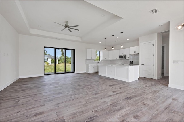 unfurnished living room with ceiling fan, light hardwood / wood-style floors, sink, and a tray ceiling