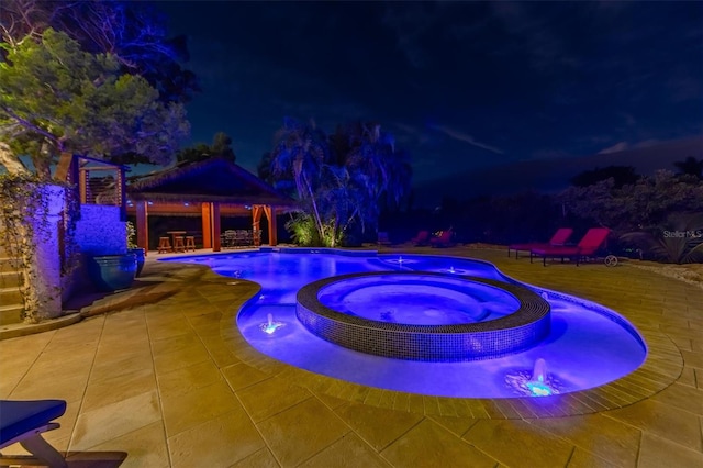 pool at night featuring a patio area, an in ground hot tub, and a gazebo