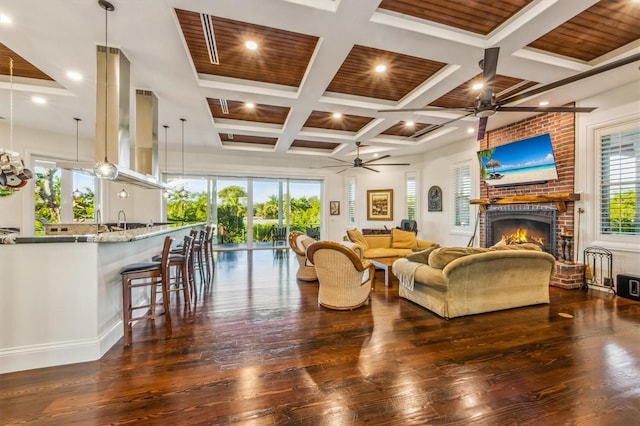 living room featuring ceiling fan, dark hardwood / wood-style flooring, beamed ceiling, coffered ceiling, and a fireplace