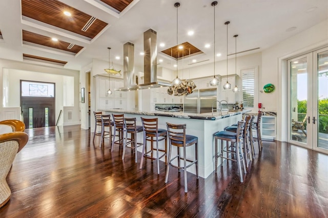 kitchen featuring light stone countertops, decorative light fixtures, stainless steel built in refrigerator, dark hardwood / wood-style flooring, and island exhaust hood