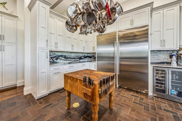 kitchen featuring built in fridge, wine cooler, white cabinets, light stone counters, and tasteful backsplash