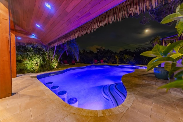 pool at night featuring a patio