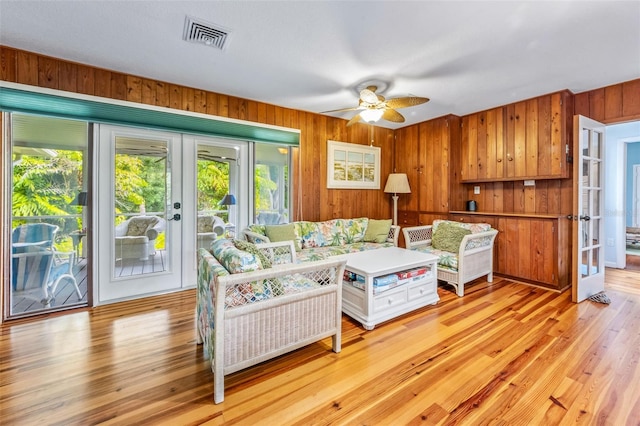 living room featuring french doors, wooden walls, ceiling fan, and light wood-type flooring