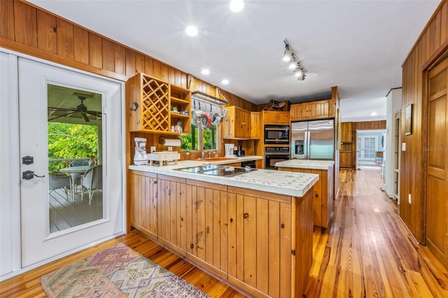 kitchen featuring wood walls, kitchen peninsula, light hardwood / wood-style flooring, black appliances, and tile counters