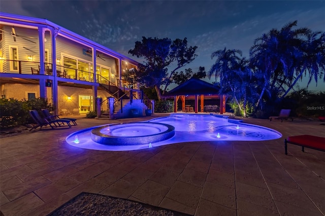 pool at twilight featuring a patio area and an in ground hot tub