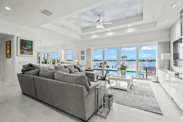 living room with a tray ceiling, ceiling fan, and a wealth of natural light