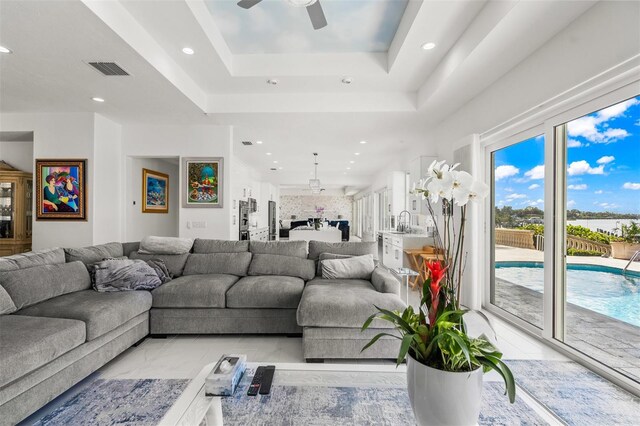 living room featuring a raised ceiling, light tile flooring, and ceiling fan