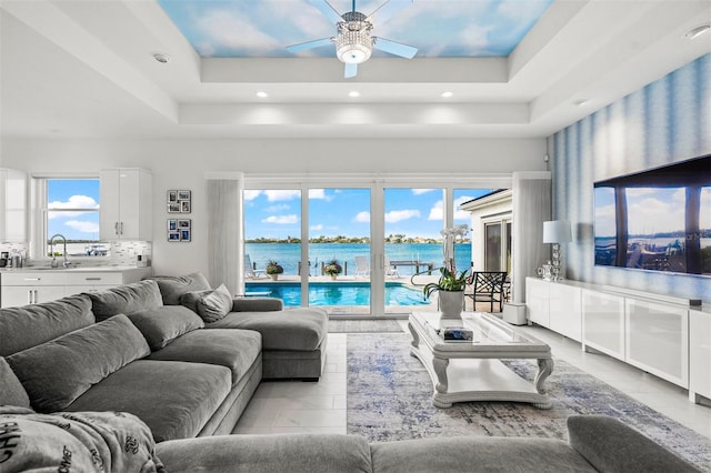 living room with a raised ceiling, light tile flooring, and ceiling fan