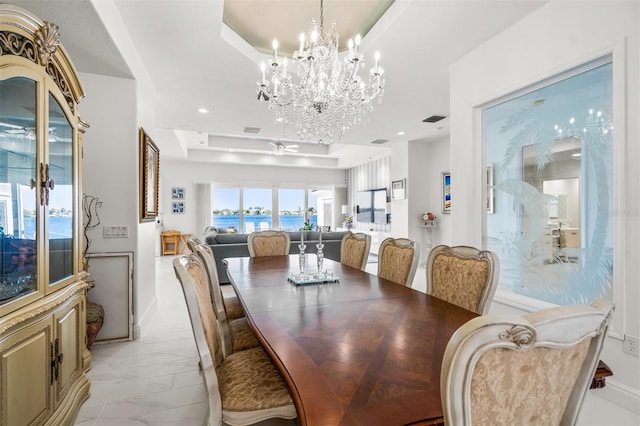 dining area featuring a raised ceiling, a water view, ceiling fan with notable chandelier, and light tile floors