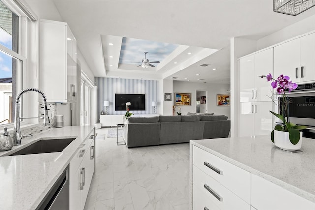 kitchen with light stone countertops, ceiling fan, light tile floors, white cabinets, and a raised ceiling