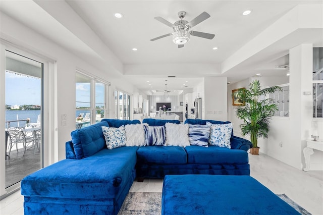 living room featuring a tray ceiling, ceiling fan with notable chandelier, and a water view