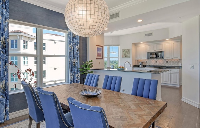 dining room with sink, crown molding, and light hardwood / wood-style flooring