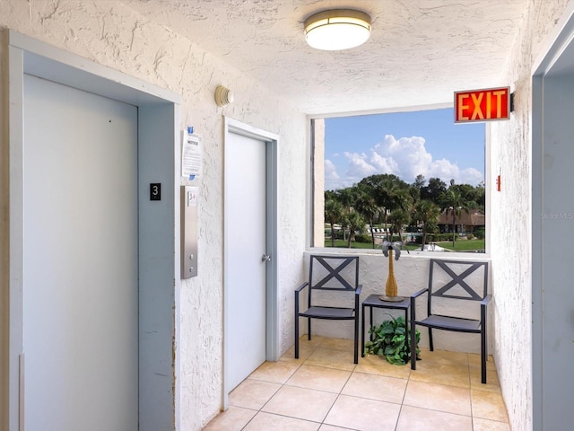 hall featuring light tile flooring, a textured ceiling, and elevator