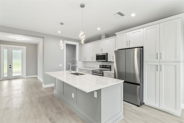 kitchen with an island with sink, stainless steel appliances, decorative light fixtures, white cabinets, and sink