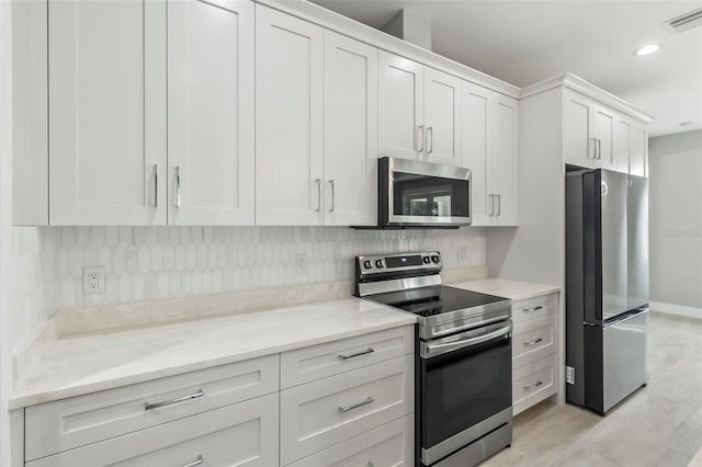 kitchen with white cabinets, backsplash, light stone counters, and stainless steel appliances