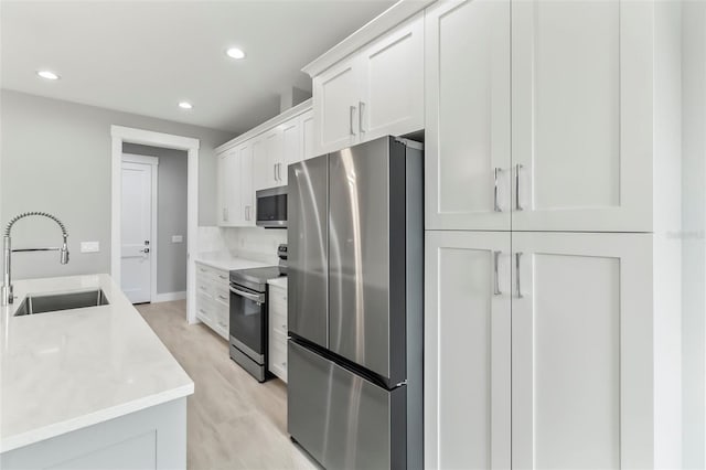 kitchen with appliances with stainless steel finishes, white cabinets, backsplash, light wood-type flooring, and sink