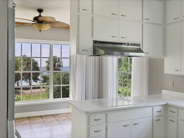 kitchen with kitchen peninsula, ceiling fan, a healthy amount of sunlight, white cabinets, and wall chimney range hood