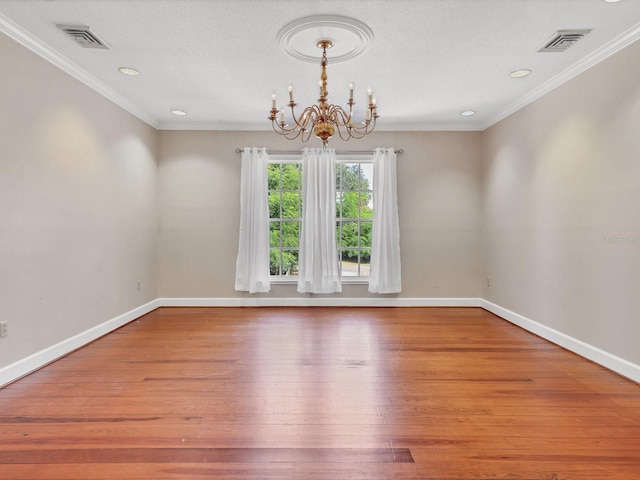 empty room featuring ornamental molding, hardwood / wood-style floors, a textured ceiling, and an inviting chandelier