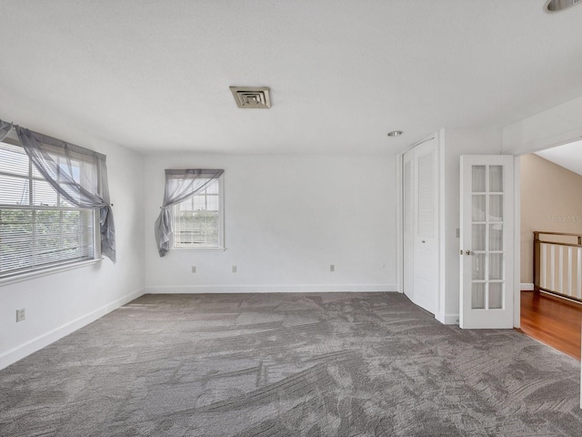 empty room with dark carpet, french doors, and a wealth of natural light