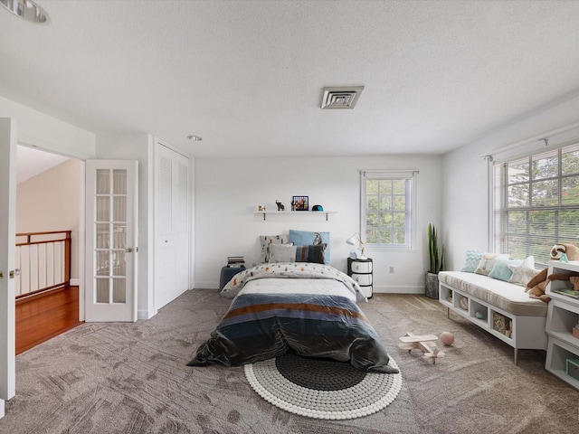 carpeted bedroom with french doors, a textured ceiling, and multiple windows