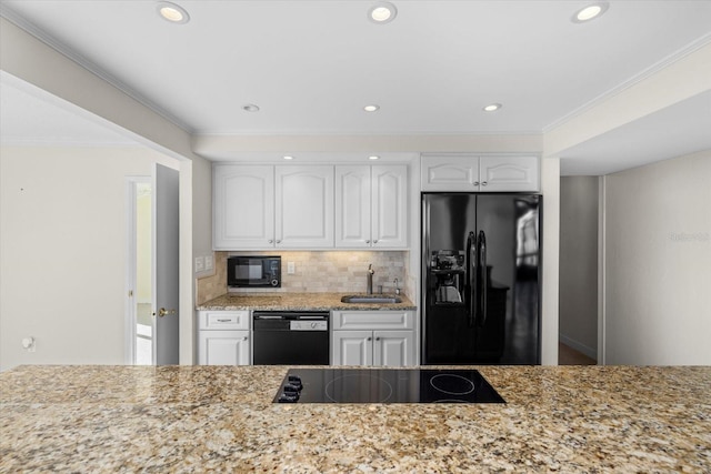 kitchen with sink, light stone counters, white cabinets, black appliances, and ornamental molding