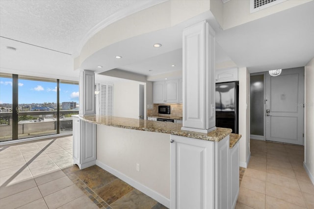 kitchen featuring light stone countertops, tasteful backsplash, a textured ceiling, white cabinets, and fridge