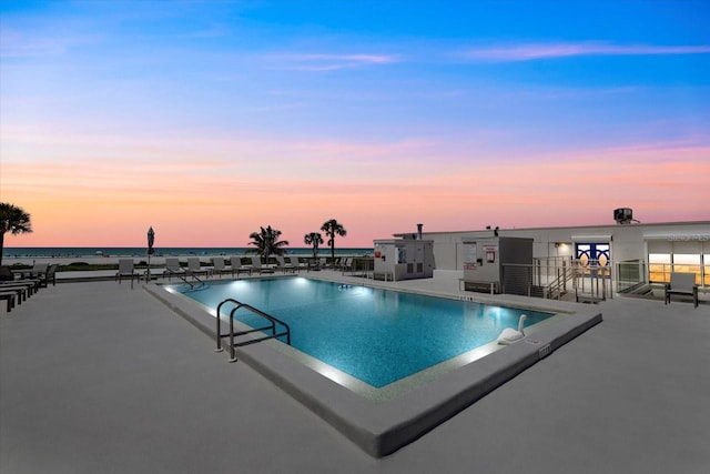 pool at dusk featuring a patio and a water view