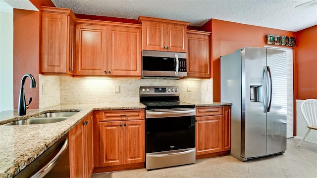 kitchen featuring light tile patterned flooring, sink, stainless steel appliances, light stone countertops, and a textured ceiling