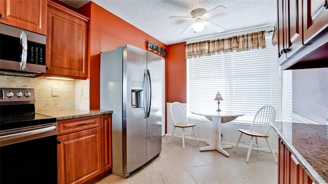 kitchen with appliances with stainless steel finishes, decorative backsplash, ceiling fan, light stone countertops, and a textured ceiling